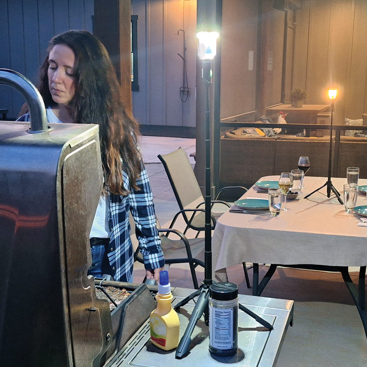 Woman grilling outdoors with a FLi-MORPHE lighting up here grilling experience. In the background, an outdoor table with place settings and wine glasses. A FLi-MORPHE set to warm light sitting in the middle of the table.